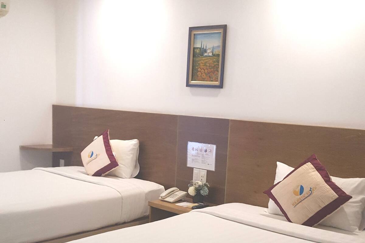A hotel room with two beds, a nightstand with a phone and a vase of flowers, and a framed picture on the wall.