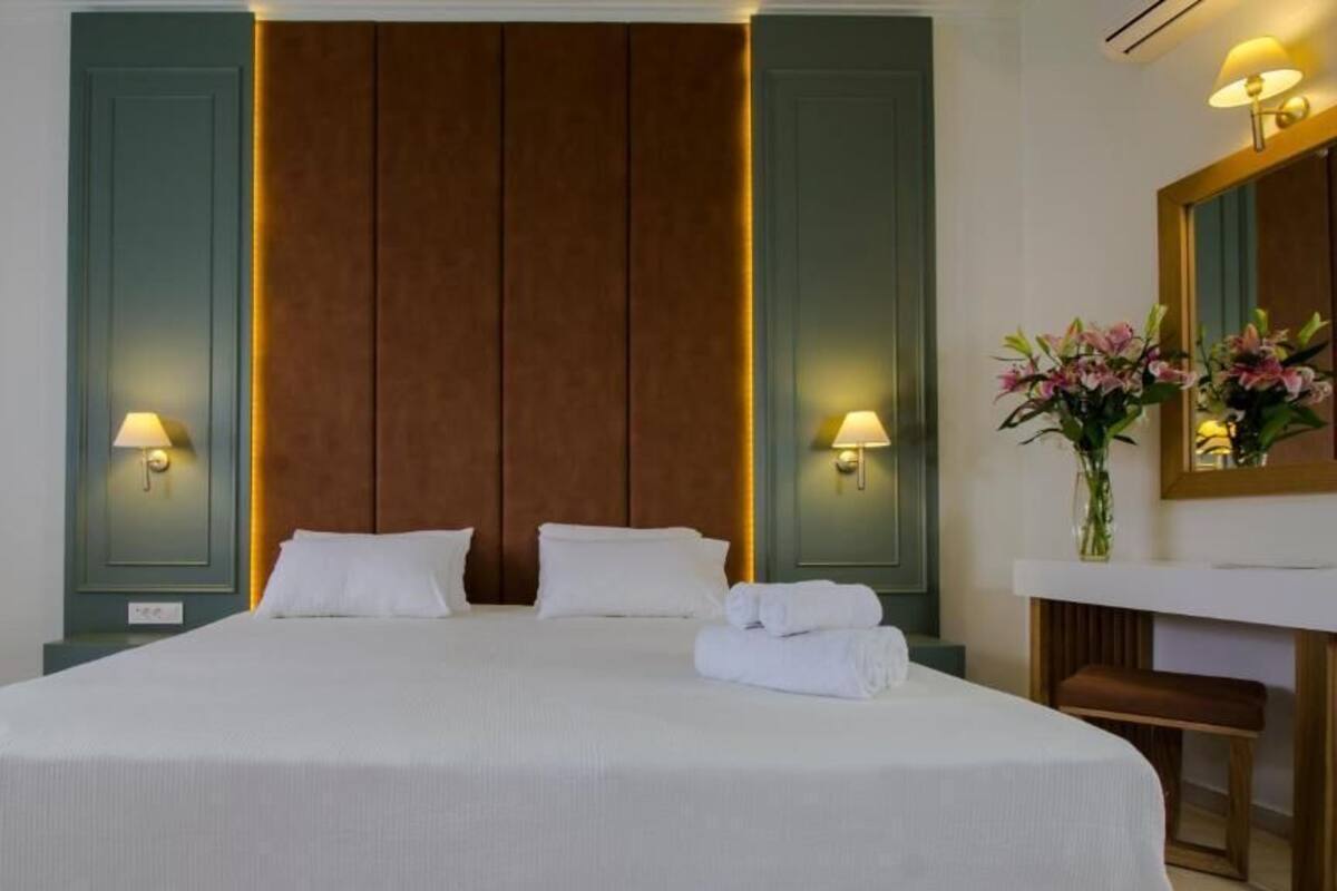 Ein Hotelzimmer mit einem großen Bett, zwei Nachttischlampen, einem Spiegel und einer Vase mit Blumen.