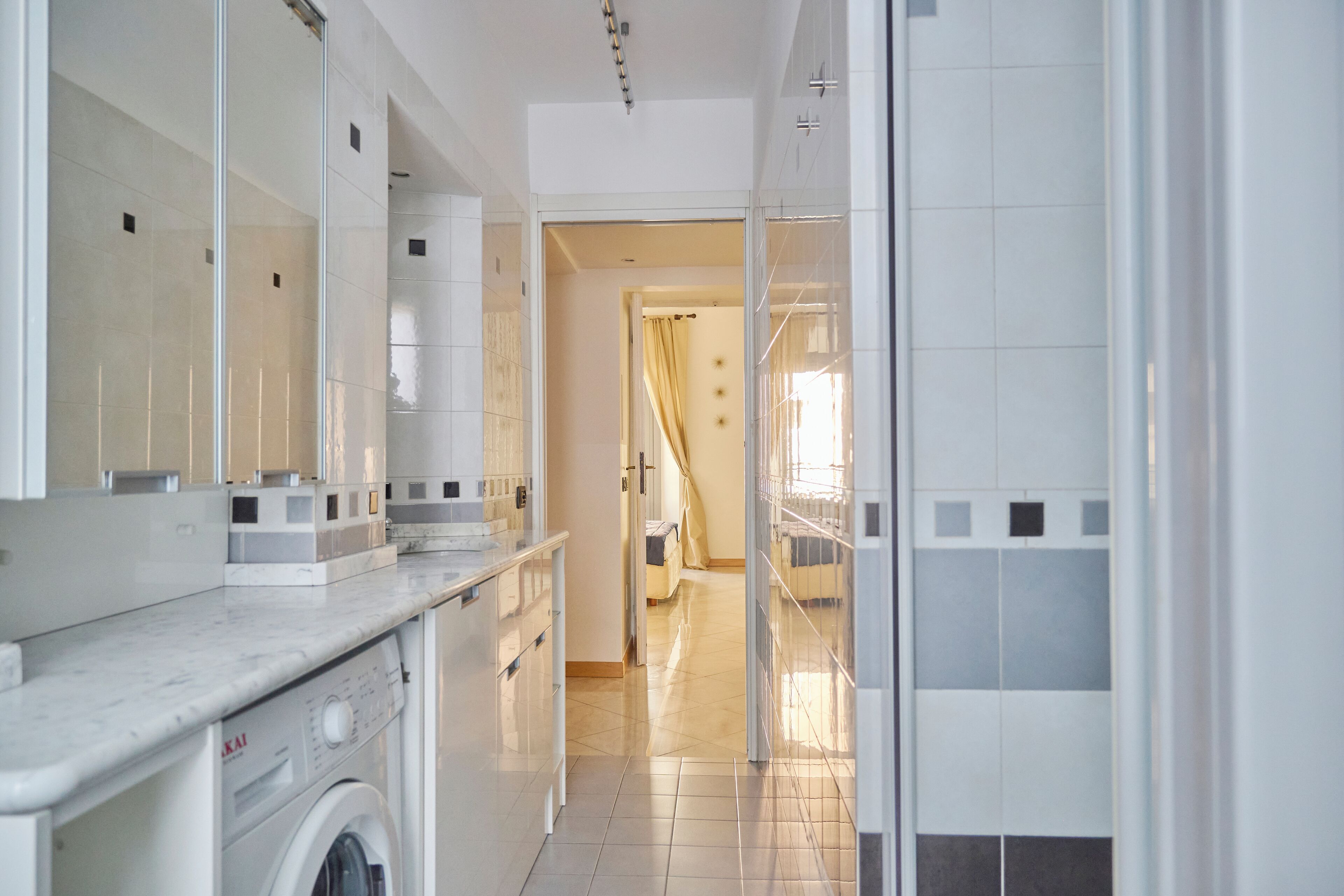 Un baño moderno con lavadora, un espejo grande y zona de ducha.