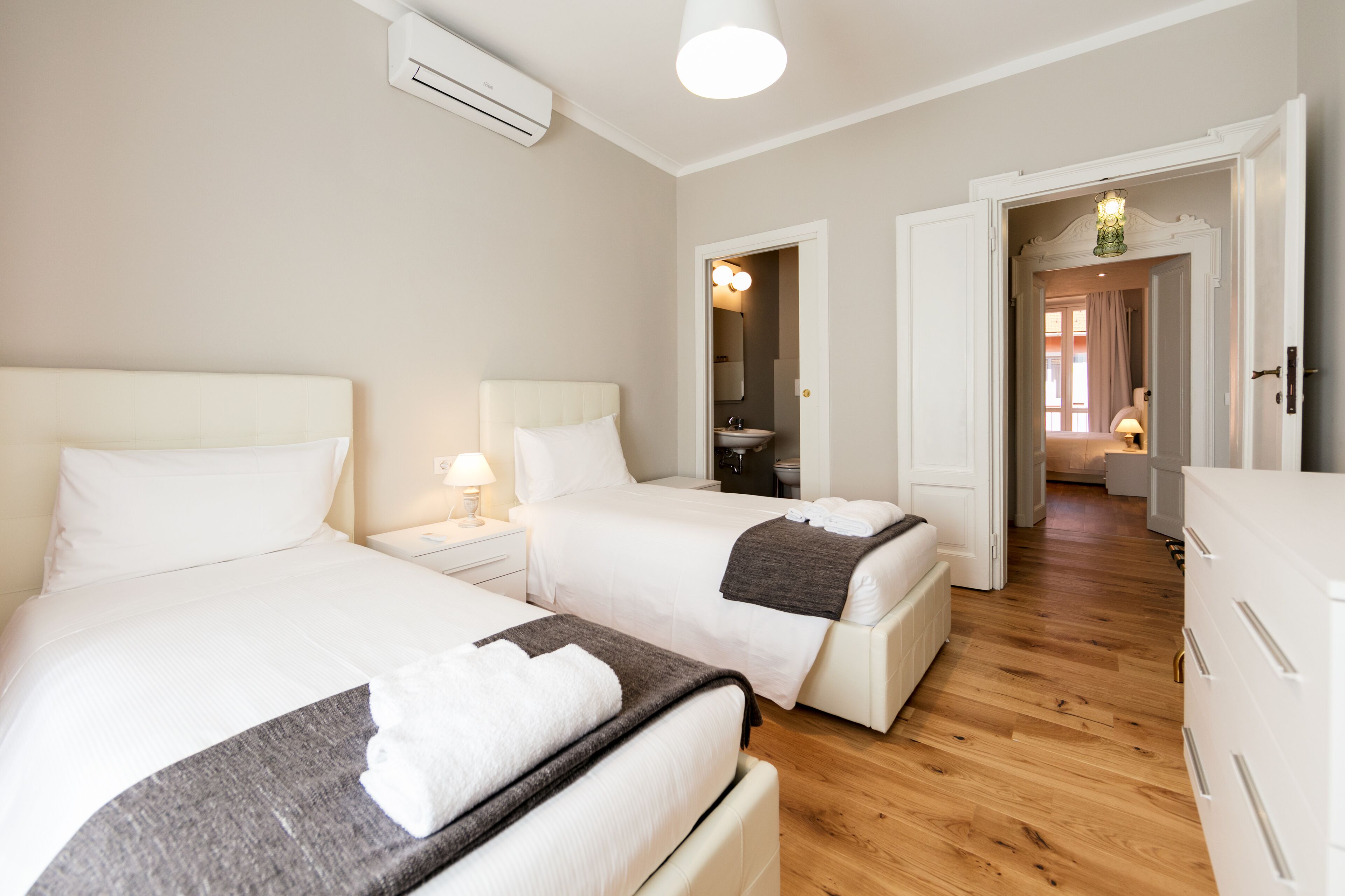 A hotel room with two beds, a bathroom, and a hallway leading to another room.