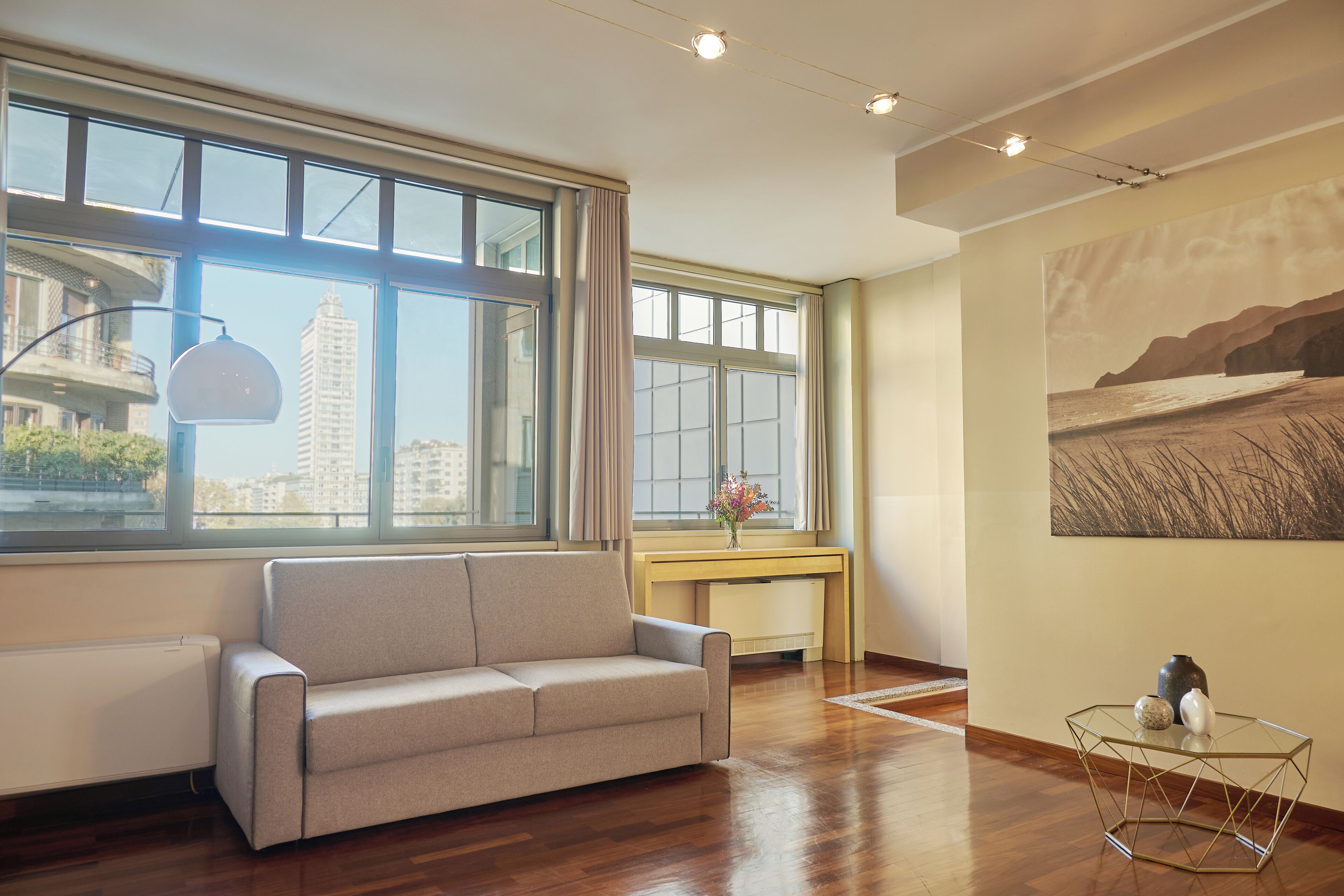 A modern living room with a sofa, a glass coffee table, and a painting on the wall.