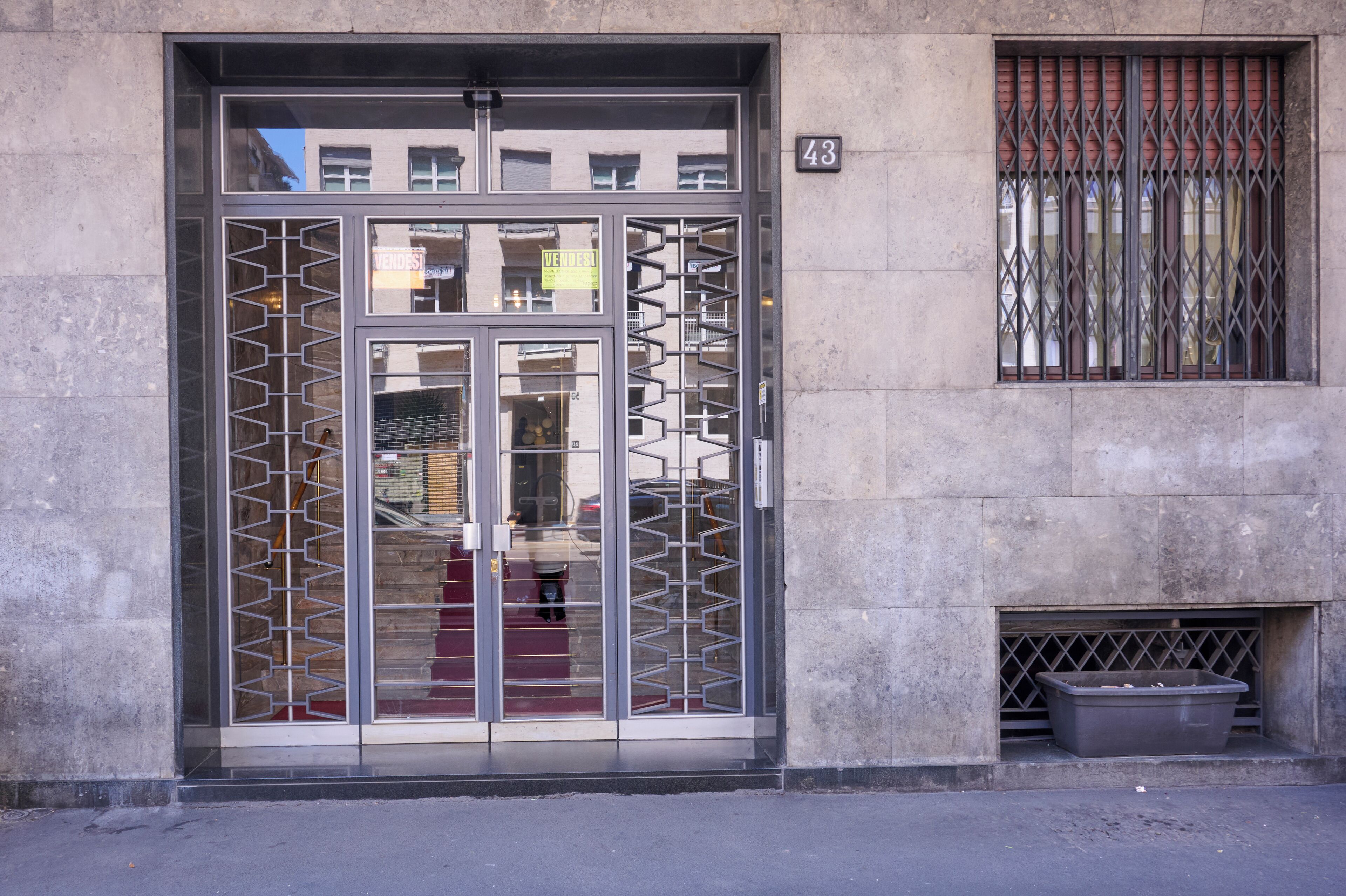 Entrada de un edificio con una verja metálica, un pequeño ventanal con barrotes y el número 43 en la pared.