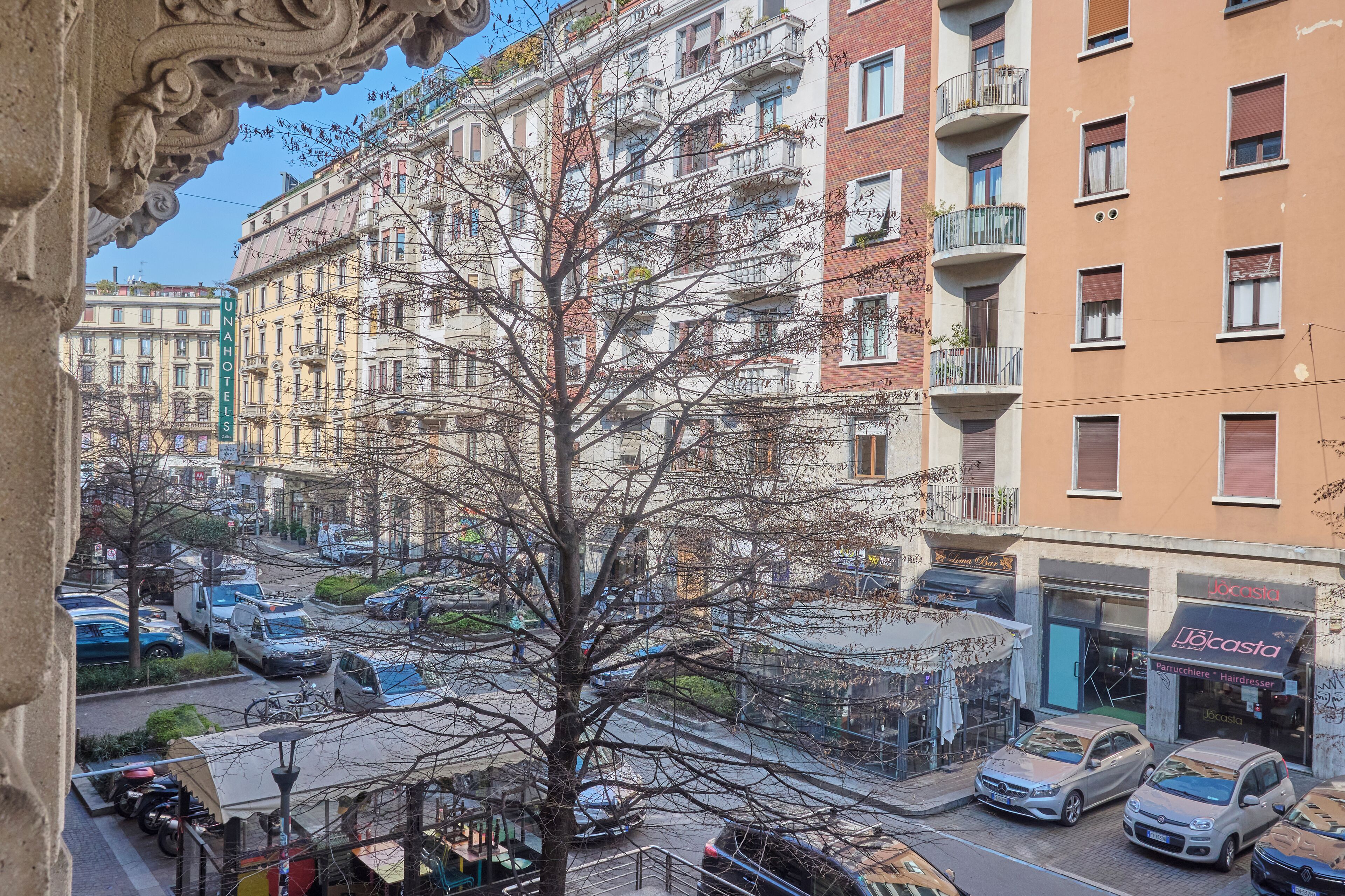 A multi-story building with balconies, a visible storefront, and parked cars.