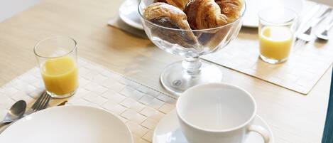 A breakfast setting with croissants, a glass of orange juice, and a cup on a table.