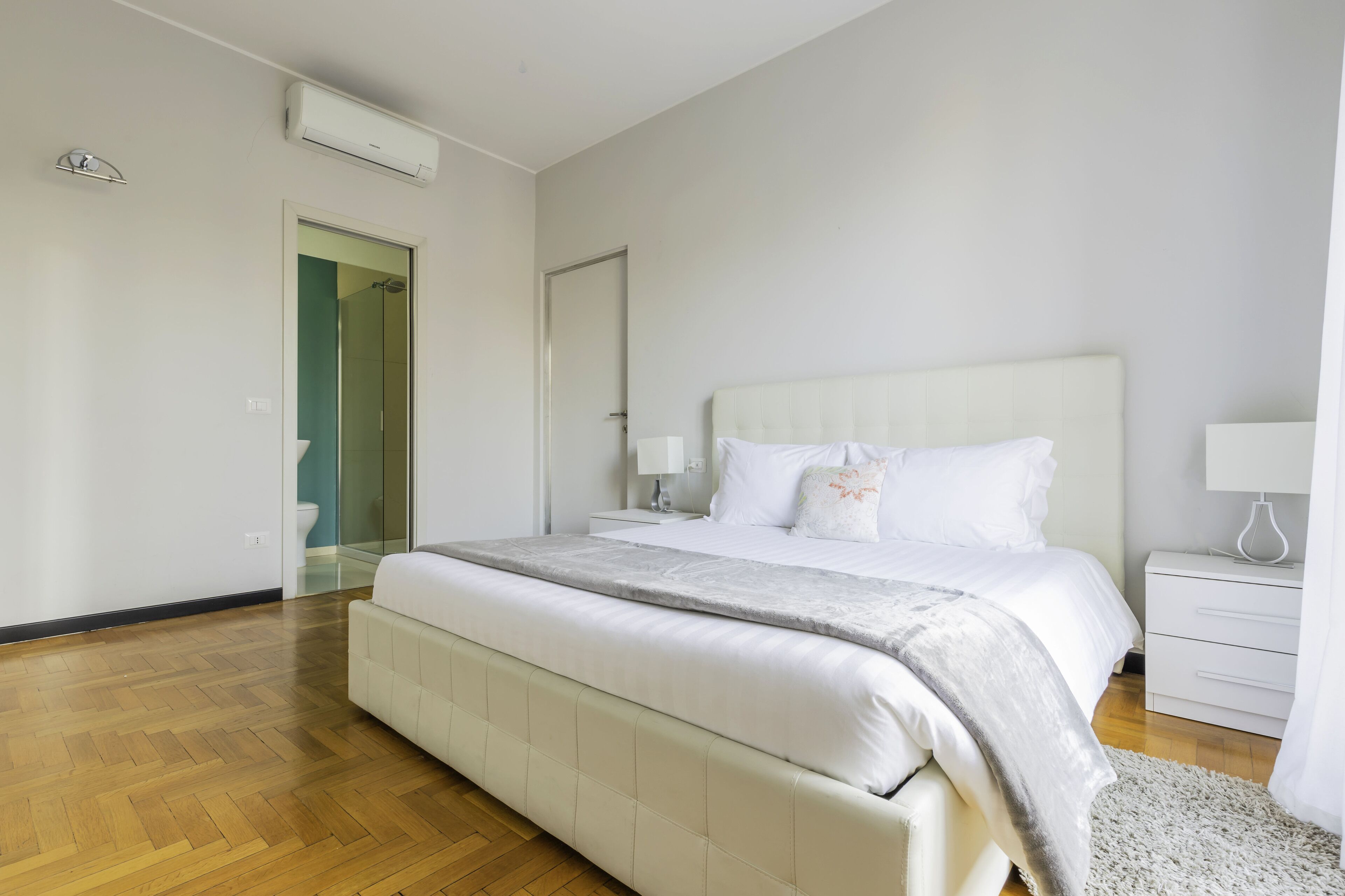 A modern bedroom with a large bed, a bedside table, a nightstand, and a walk-in closet.