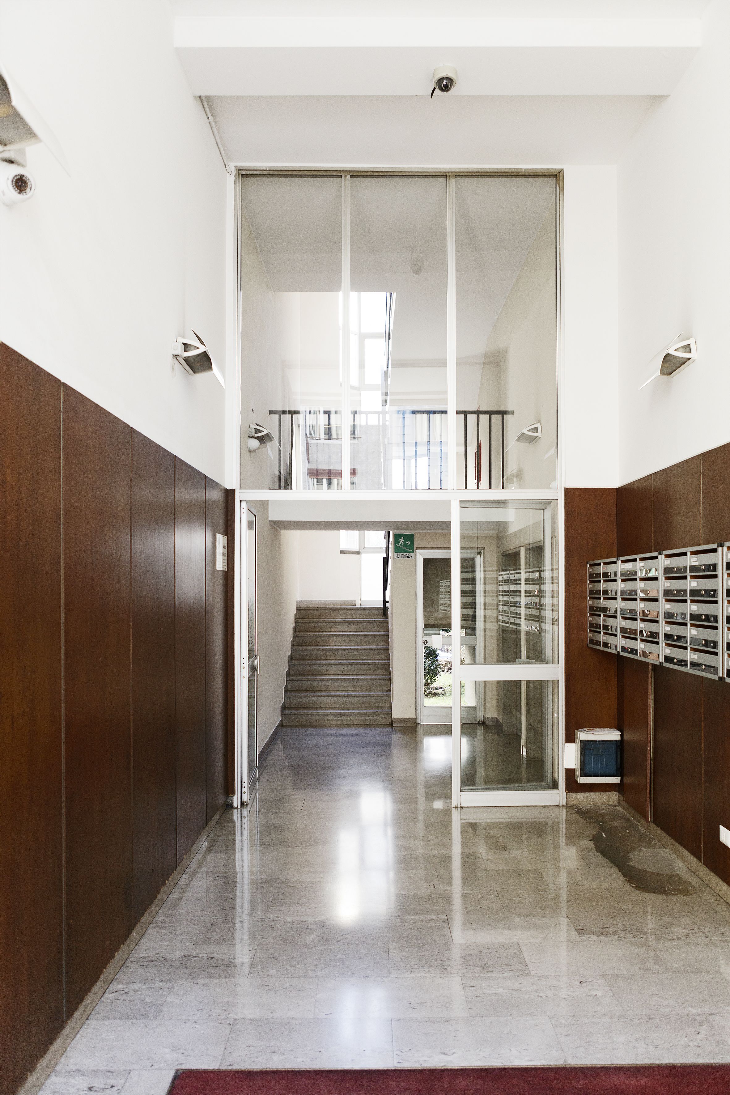 A clean, modern lobby with a marble floor, a staircase leading to an upper level, and a glass door entrance.