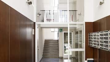 Un vestíbulo moderno y luminoso con suelo de mármol, una escalera que sube a un nivel superior y un acceso por puerta de vidrio.