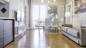 A modern living room with a sofa, chairs, a dining table, and a kitchen area with a refrigerator. - Milan Retreats - Central Station (Milan)