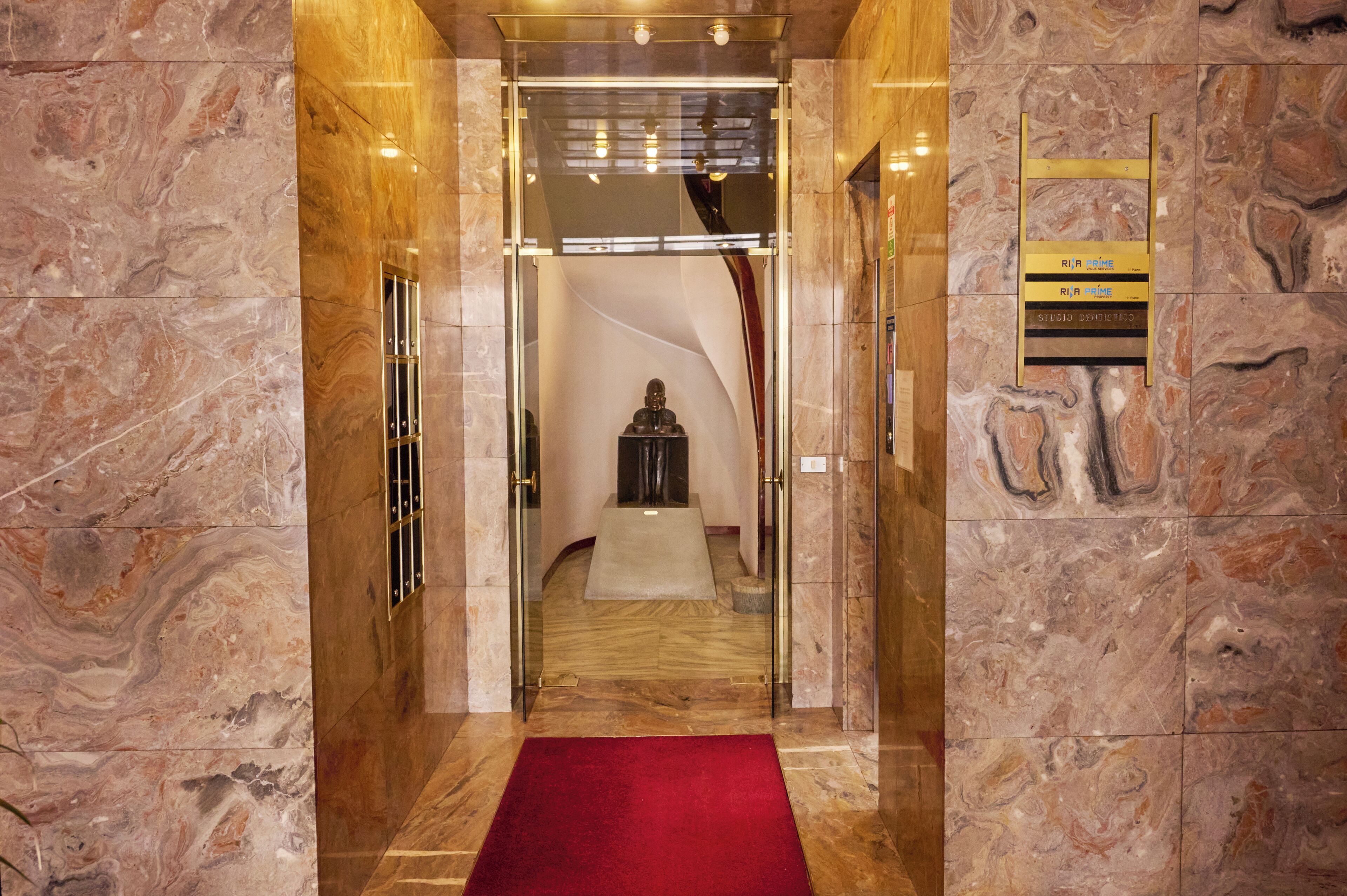 Hall de entrada com piso de mármore e um tapete vermelho que leva à área de recepção.