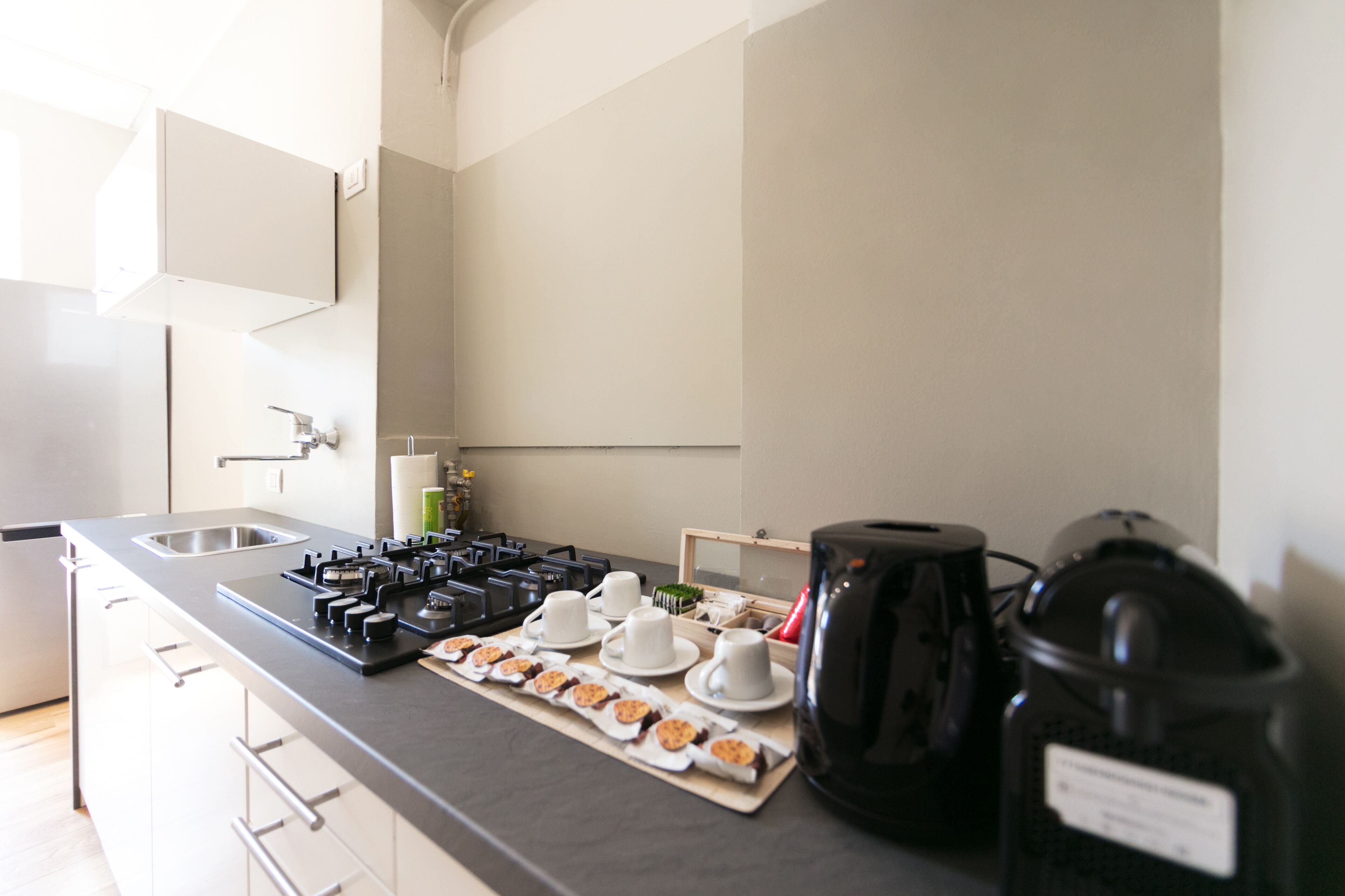 A modern kitchen with a gas stove, a sink, and a coffee station with cups and a kettle.