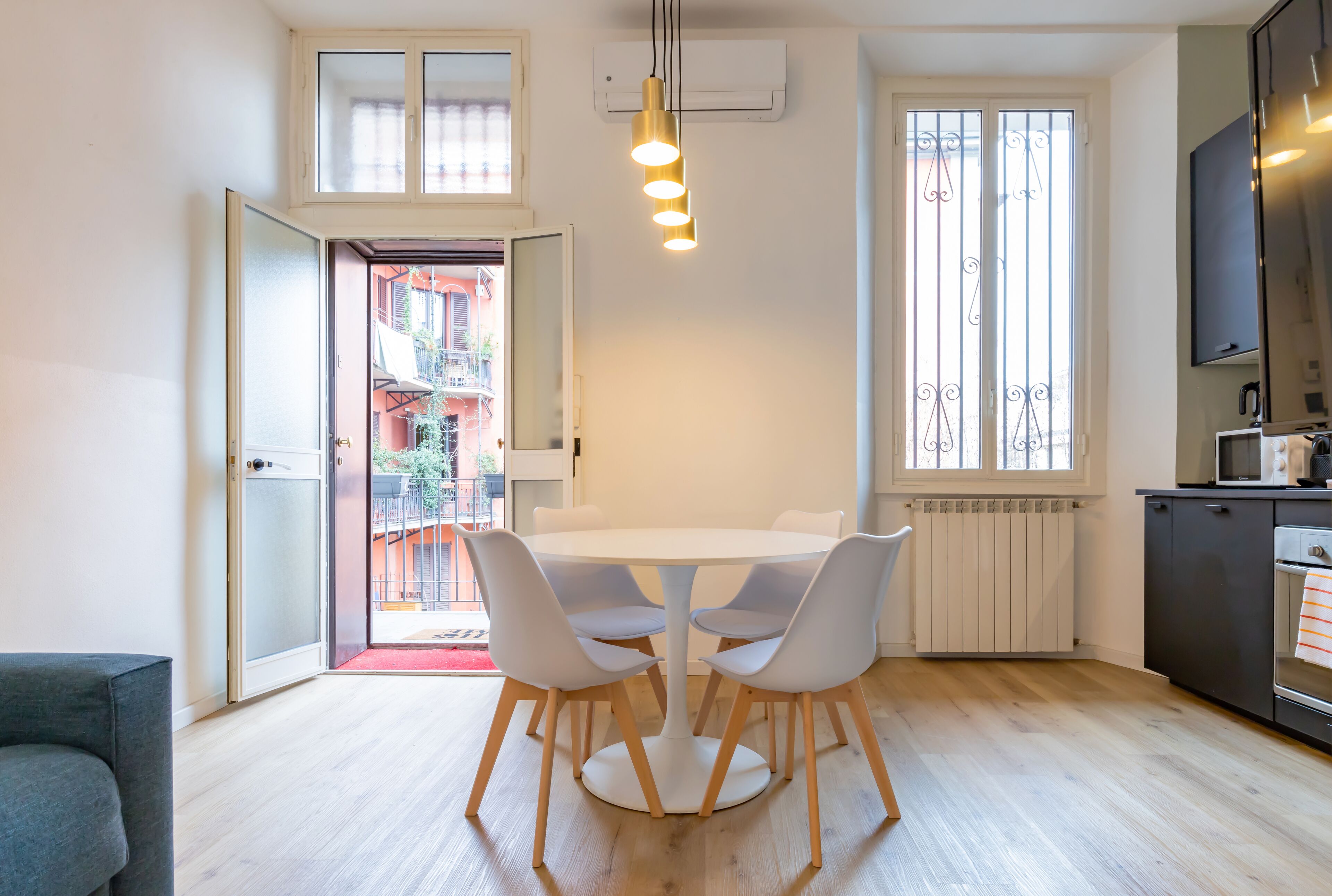 A modern kitchen with a dining area, featuring a round table with chairs, a built-in oven, and a large window with decorative iron bars.