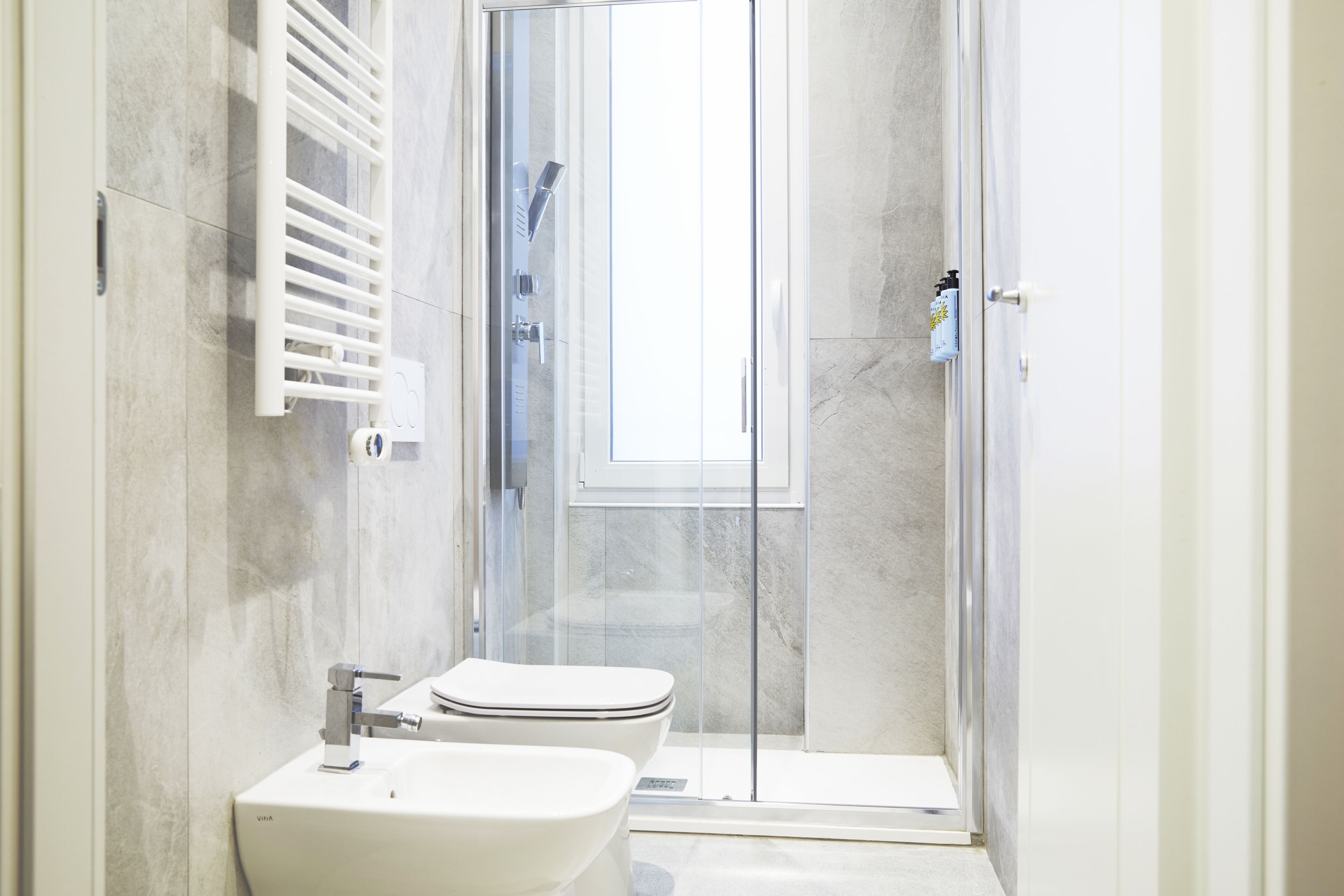 Et moderne badeværelse med en glasbrusekabine, en hvid vask og et toilet.