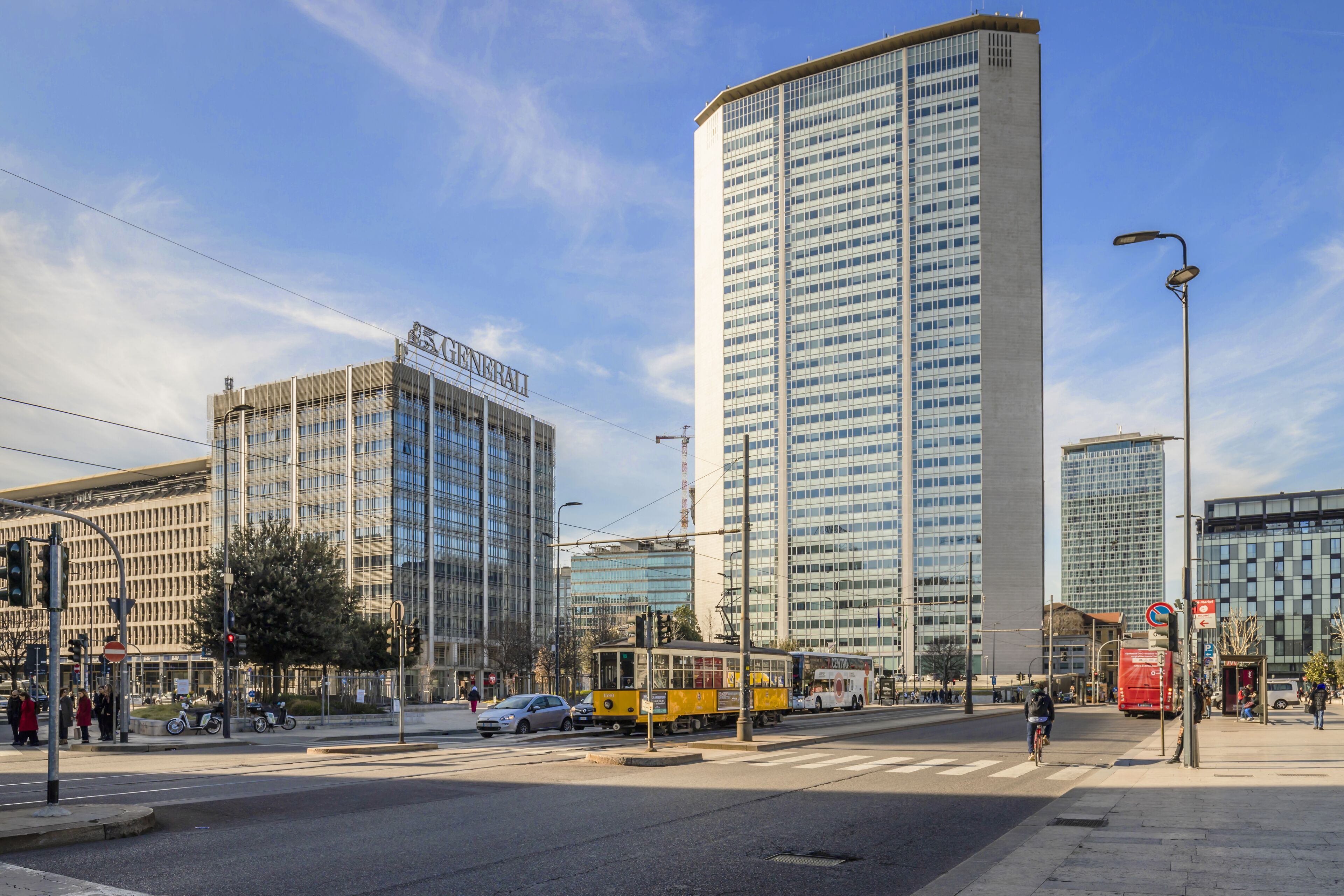 Een stadsplein met moderne gebouwen, een tram en een voetgangersoversteek.