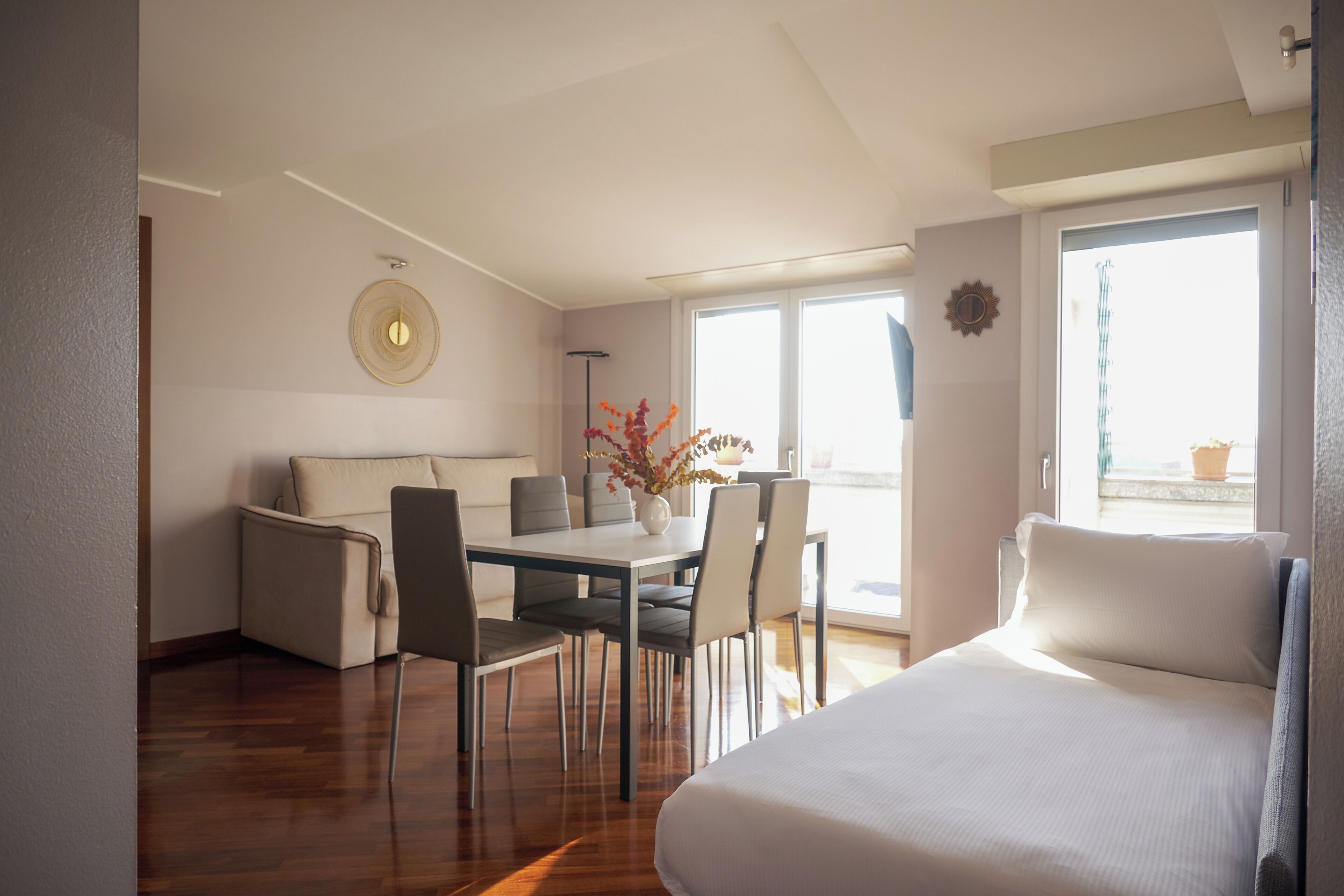 Una moderna camera d'hotel con un letto grande, un'area pranzo con tavolo e sedie, e vista all'esterno attraverso un'ampia finestra.