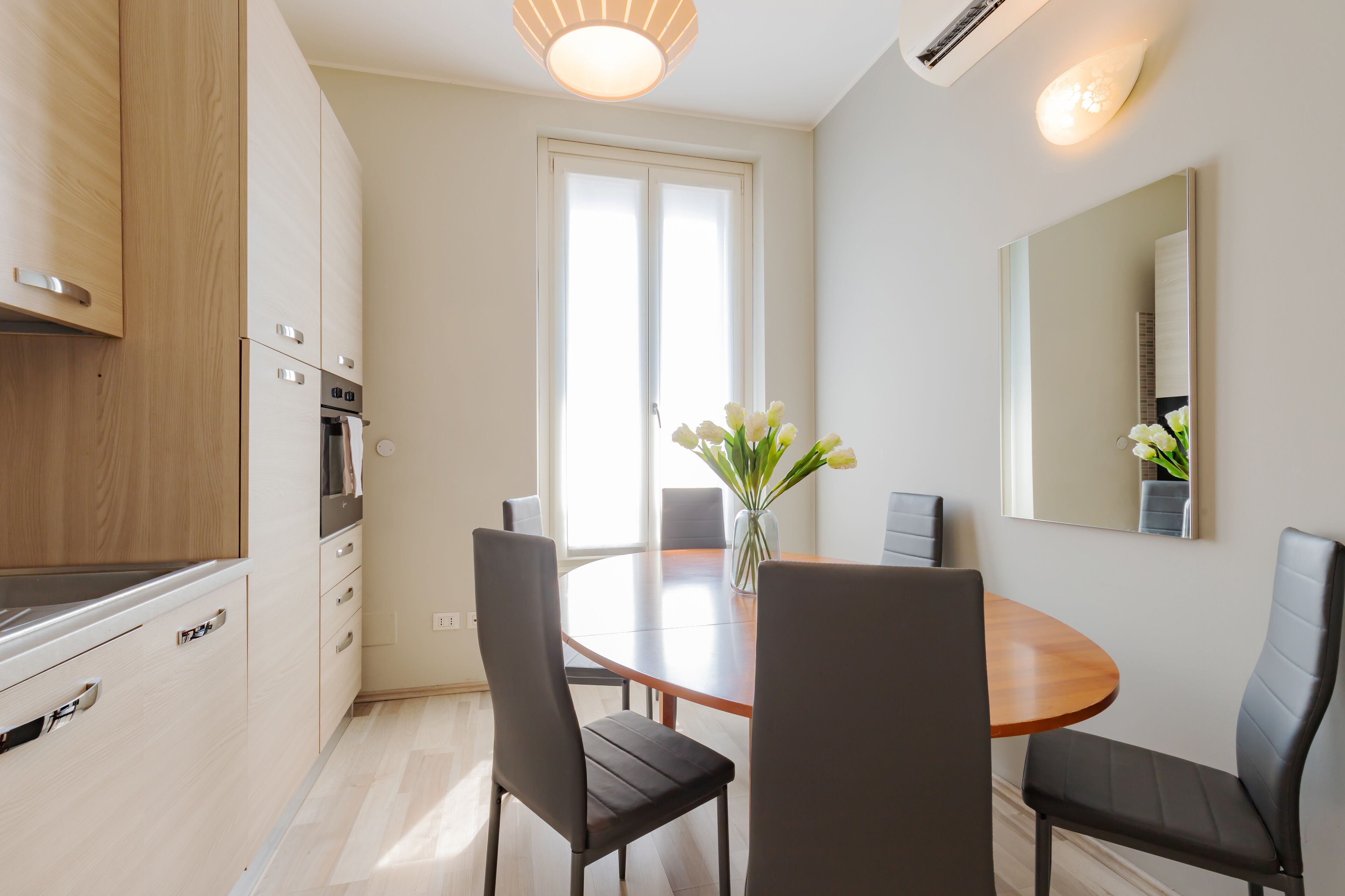 Une cuisine moderne avec des meubles en bois, un four encastré et un coin repas comprenant une table ronde et quatre chaises.