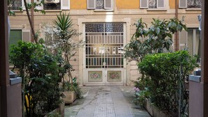 A narrow alleyway with potted plants on either side, leading to a building with a decorative gate and shutters. - Milan Retreats - Central Station (Milan)