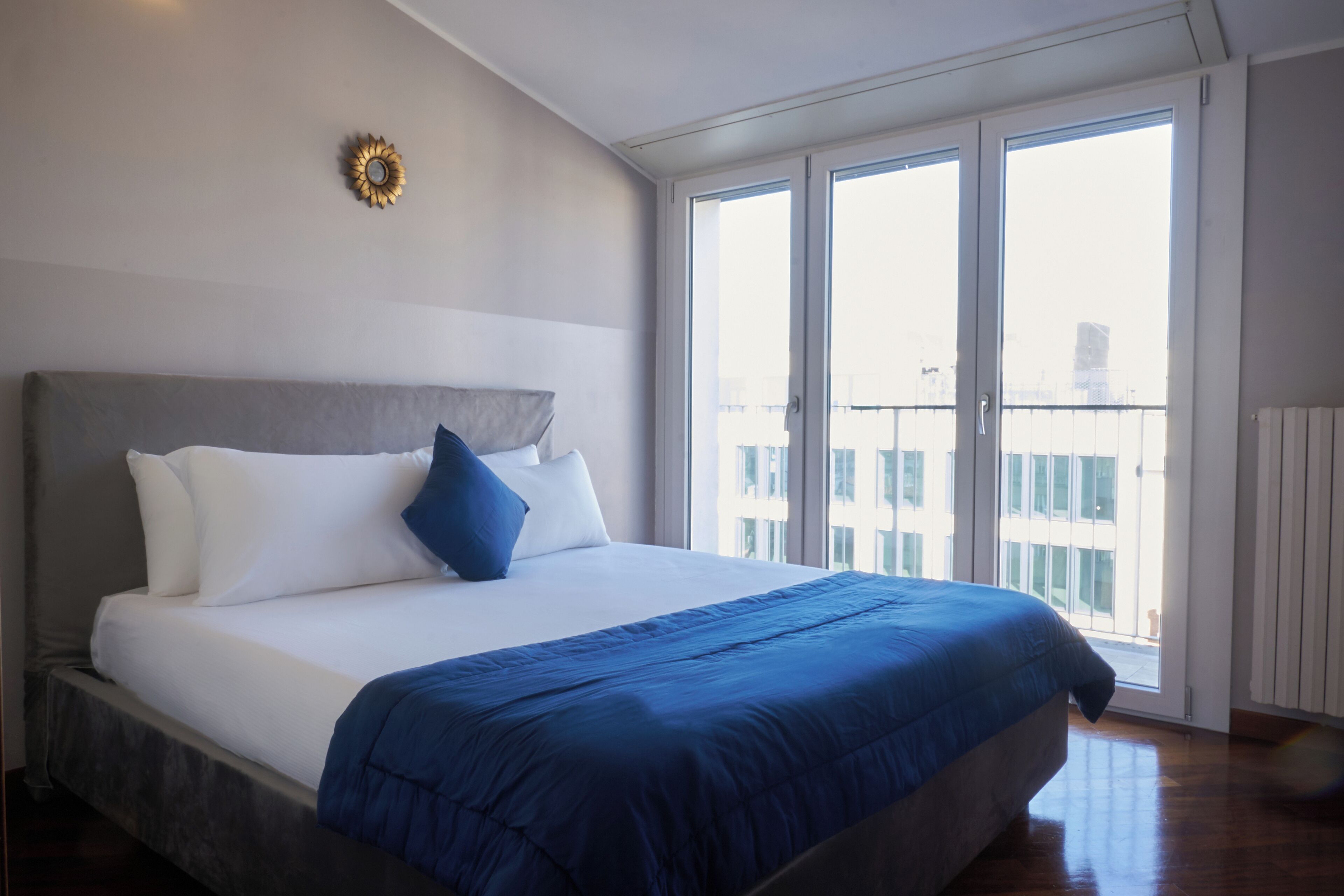 Une chambre avec un grand lit, une vue sur la ville grâce à une porte coulissante, et un élément décoratif mural.