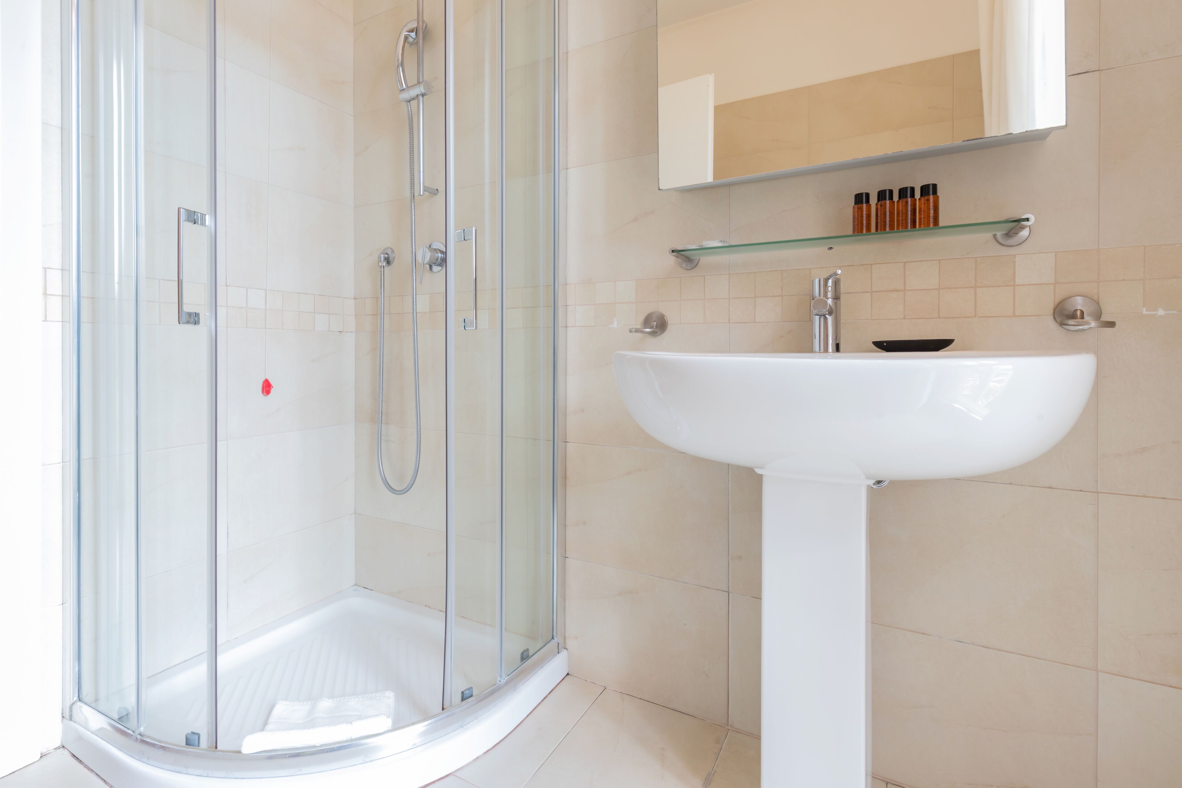 A modern bathroom with a glass-enclosed shower, a white pedestal sink, and a mirror above the sink.