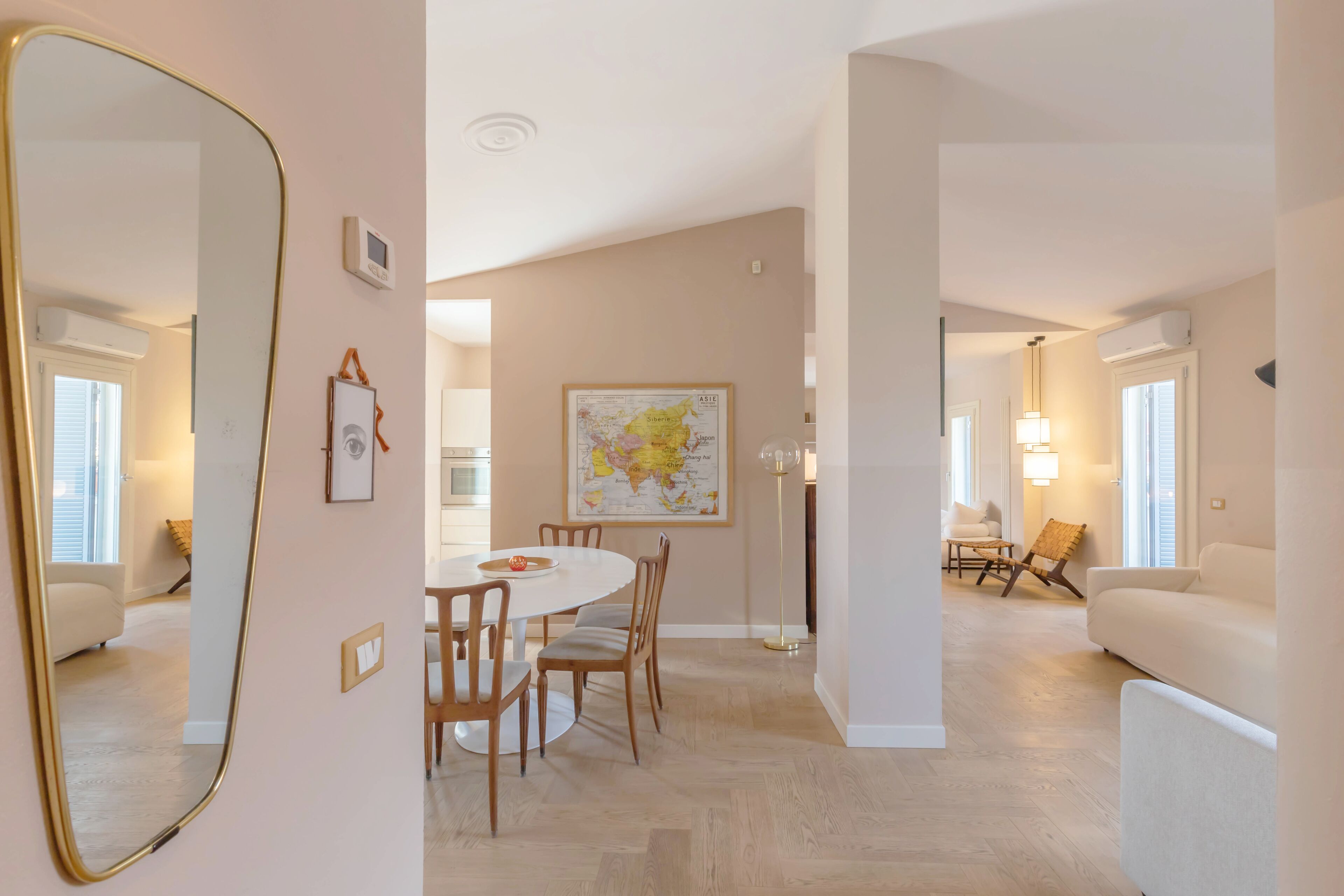 Un salón espacioso con una mesa redonda de comedor, sillas de madera, un gran mapa mundial en la pared y una lámpara moderna.
