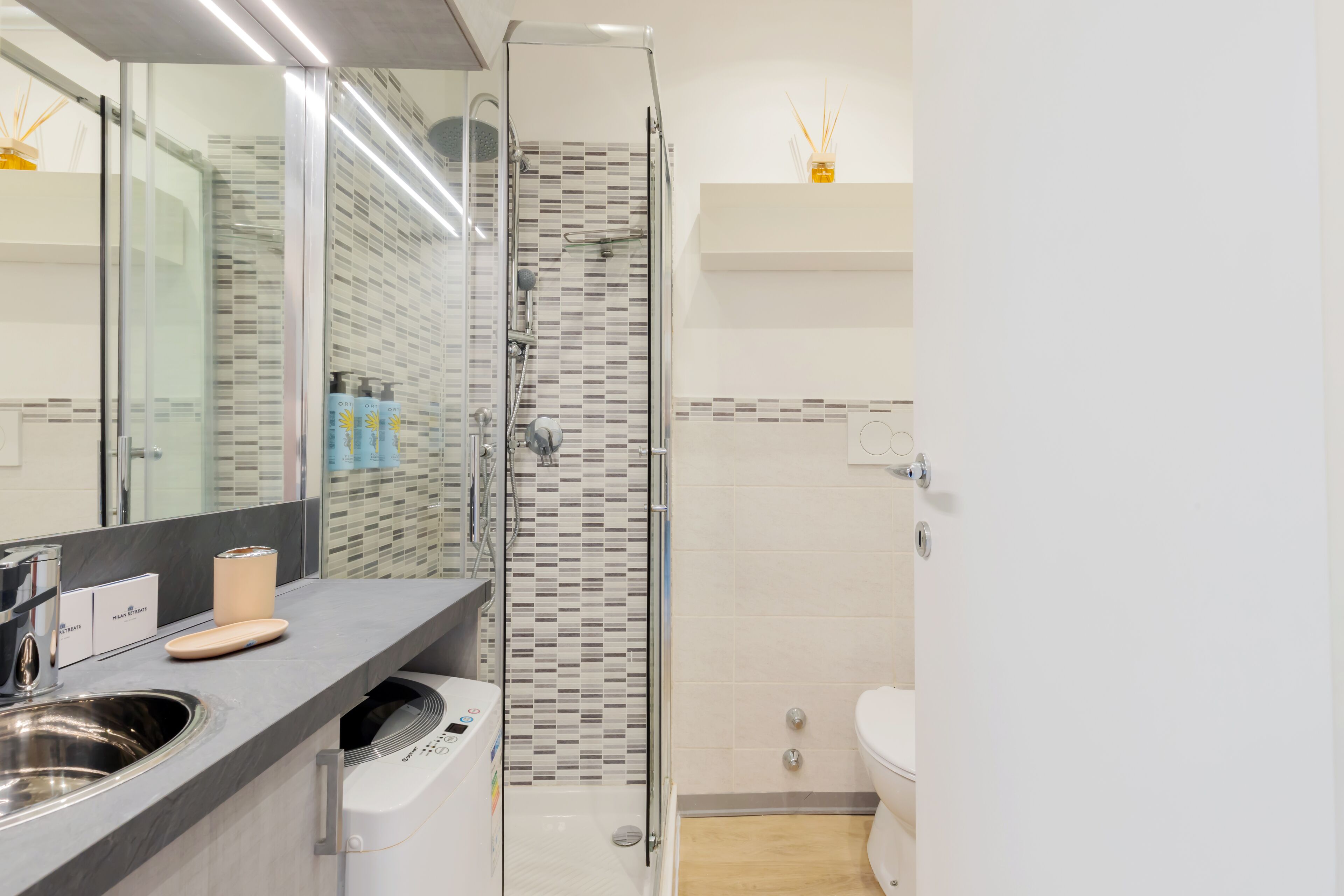 Un baño moderno con cabina de ducha de vidrio, un lavabo con dispensador de jabón y un inodoro.