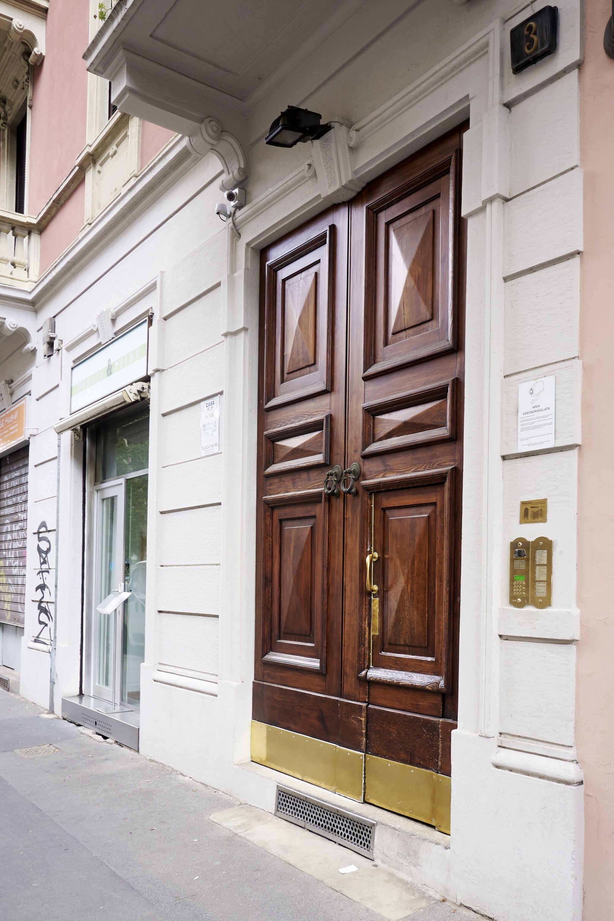 Una puerta doble de madera con un picaporte de latón, una placa con un número y una pequeña señal encima.