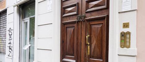 Una puerta doble de madera con un picaporte de latón, una placa con un número y una pequeña señal encima.