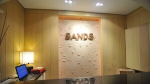 A reception desk with a laptop, a lamp, and a wall with the word "SANDS" in the center. - Boracay Sands Hotel (Boracay Island)