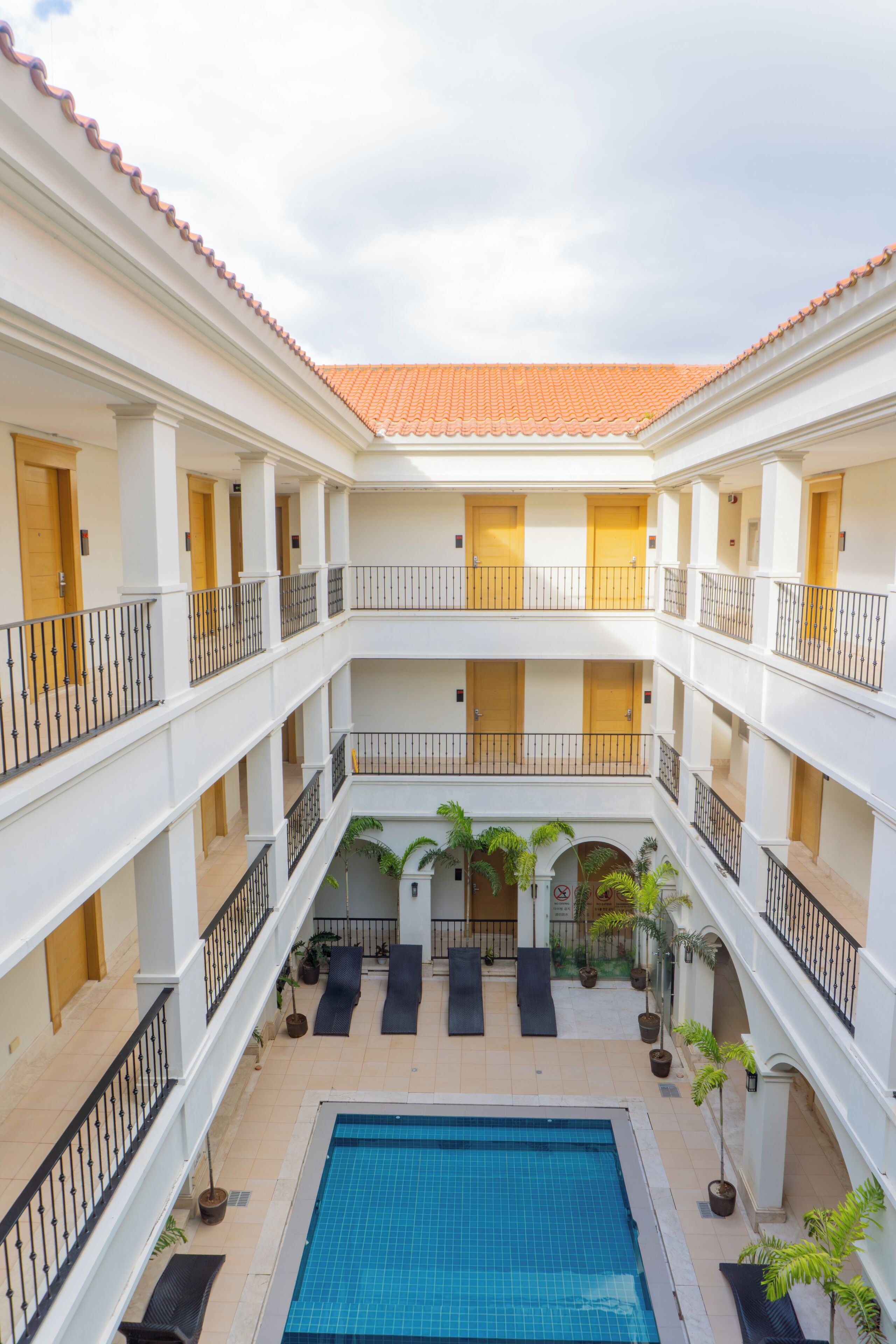A multi-level hotel atrium with a central swimming pool, balconies, and potted plants.