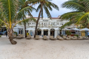 Un hotel frente a la playa con palmeras, tumbonas y sombrillas.