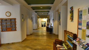 A hallway with a checkered floor, a wooden bench with magazines, a clock on the wall, and framed pictures. - Hotel Helenenburg (Bad Gastein)