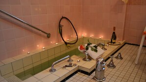 A bathroom with a bathtub, a towel rack, a bottle of champagne, and candles. - Hotel Helenenburg (Bad Gastein)