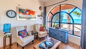A living room with a large window, a clock, a painting, and a water dispenser. - Casa Kootenay Waterfront BnB (La Paz)
