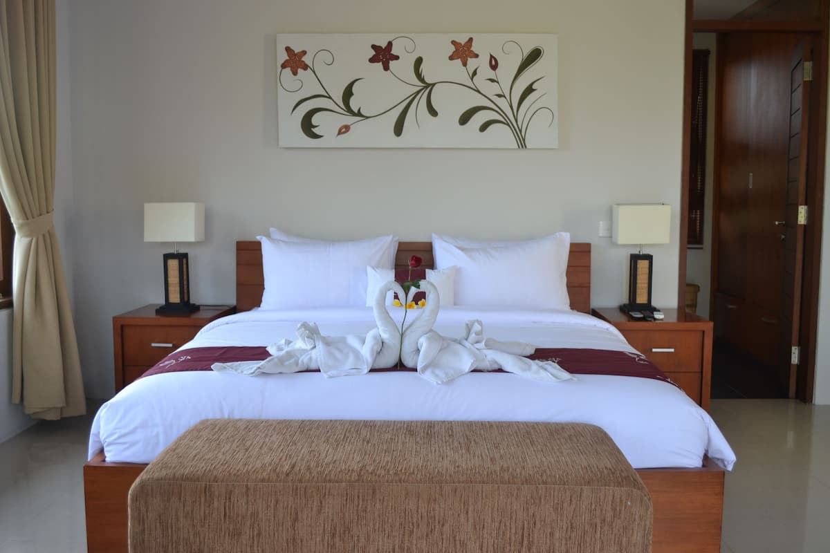 Cama bem arrumada com decoração de cisne, mesa de cabeceira com abajur e uma obra de arte na parede.