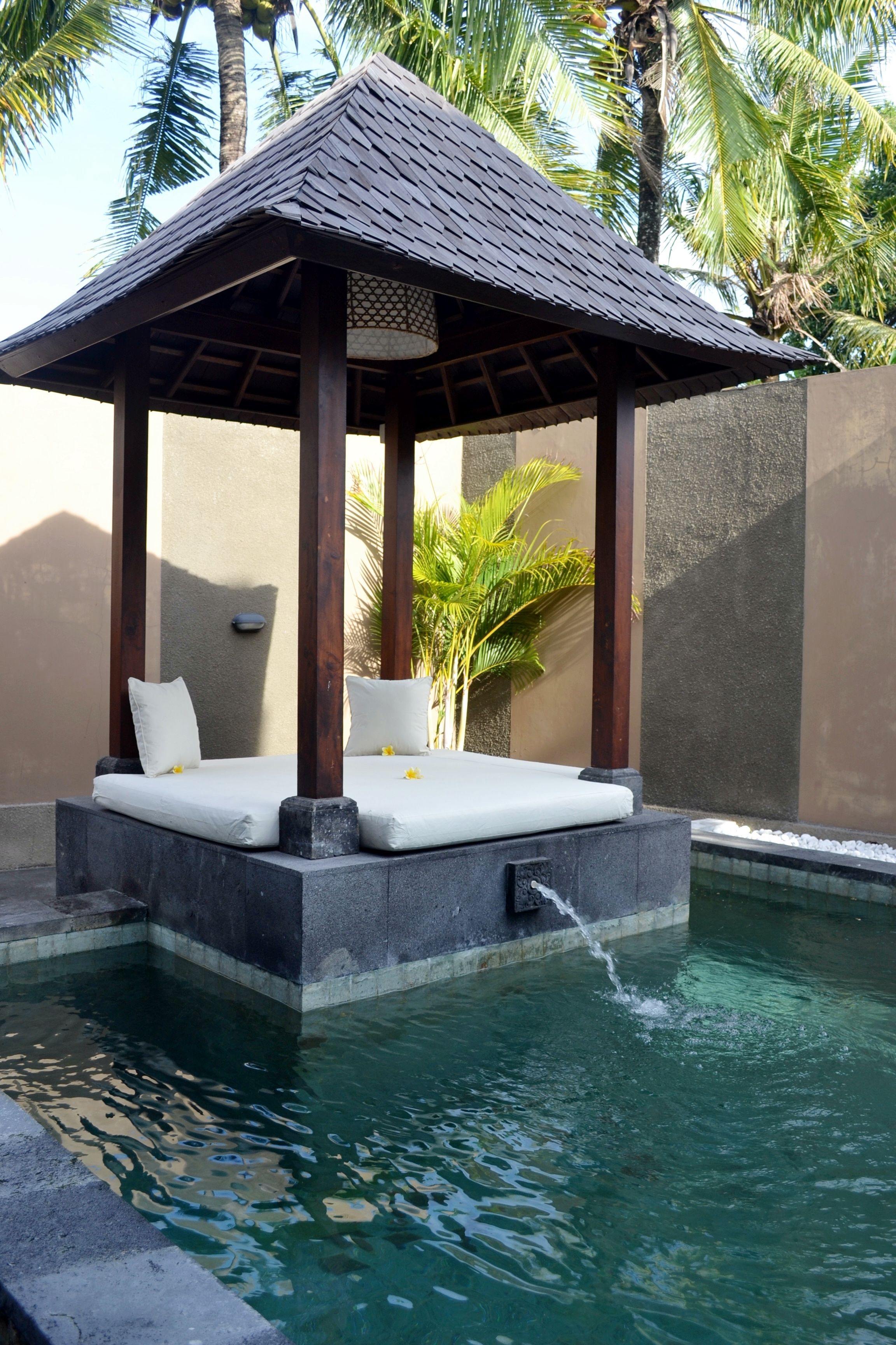 A pool with a wooden gazebo seating area, surrounded by palm trees.