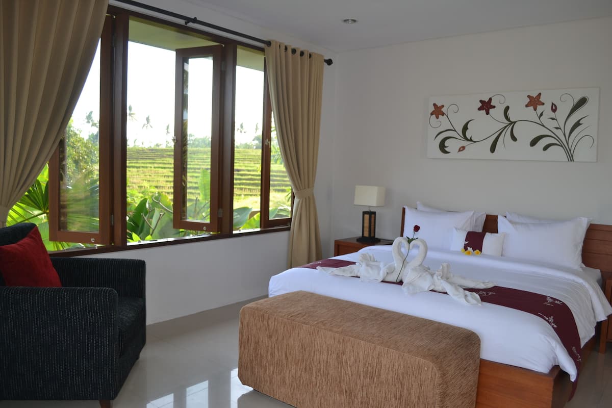 Quarto de hotel com uma cama grande, um sofá e vista para uma paisagem verde pela janela.