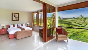 A bedroom with a large bed, a nightstand, a bench, a chair, and a sliding glass door leading to a balcony with a view of a green landscape. - Villa Lea (Tabanan)