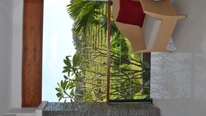 A room with a large window, a woven chair with a red cushion, and a view of greenery outside. - Villa Lea (Tabanan)