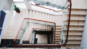A modern interior with a glass staircase leading to a lower level, a potted plant, and a marble floor. - Tebu Hotel Bandung (Bandung)