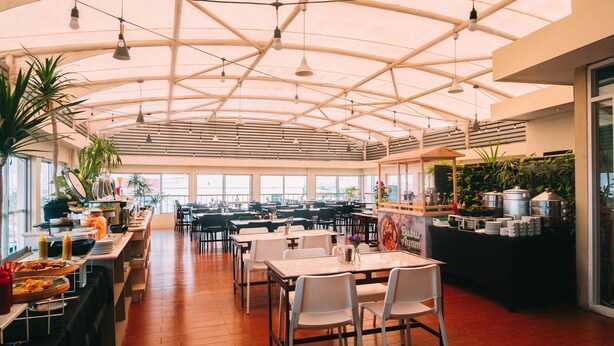 A spacious indoor dining area with high ceilings, multiple tables and chairs, and a variety of food and drink stations. - Tebu Hotel Bandung (Bandung)