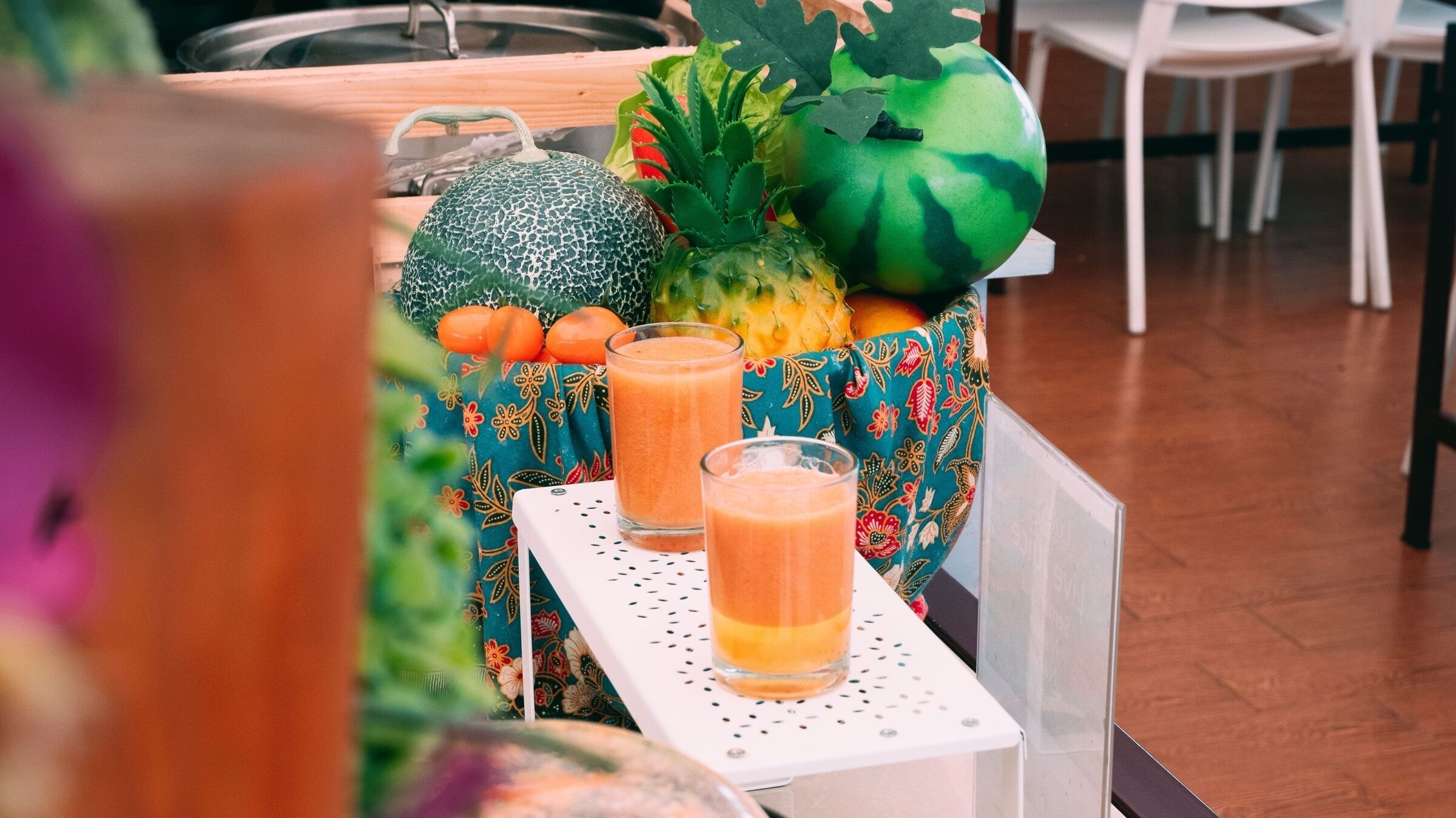 Uma mesa com uma bandeja de frutas frescas e dois copos de suco de laranja.