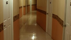Un pasillo con puertas a ambos lados que conduce a un vestíbulo con suelo de baldosas y una lámpara en el techo.