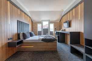 Quarto de hotel moderno com cama, estantes embutidas, televisão e vista para a paisagem urbana.