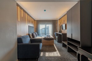 Una habitación de hotel moderna con sofá, cama, televisión y escritorio.