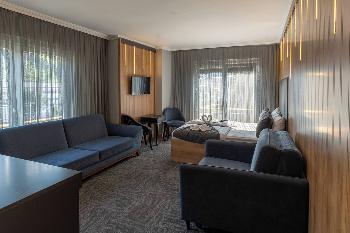 Una habitación de hotel moderna con sofá, sillón y cama con cabecera de madera.