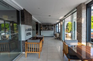 Interior moderno de un hotel con un lobby amplio, muebles de madera y ventanas grandes que ofrecen vistas al exterior.