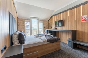 Una habitación de hotel moderna con cama, televisor, pared de madera y balcón con vistas.