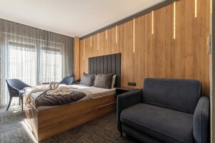 Una habitación de hotel moderna con cabecera de madera, una cama, un sofá gris y un escritorio.
