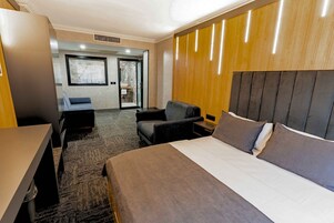 Habitación de hotel con cama, escritorio, silla, una mesita pequeña y baño visible a través de una puerta abierta.