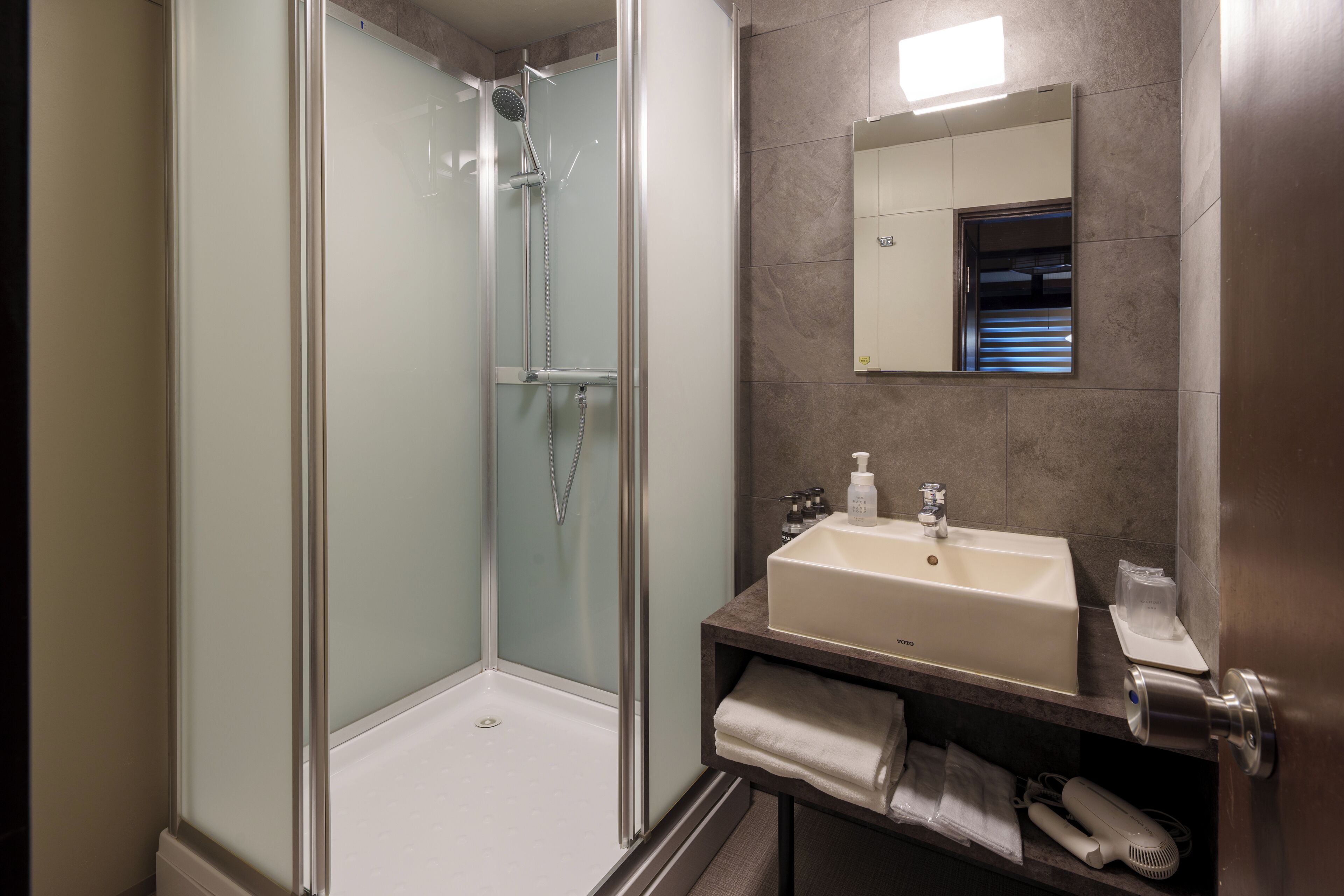 A modern bathroom with a glass-enclosed shower, a white sink, and a mirror above it.