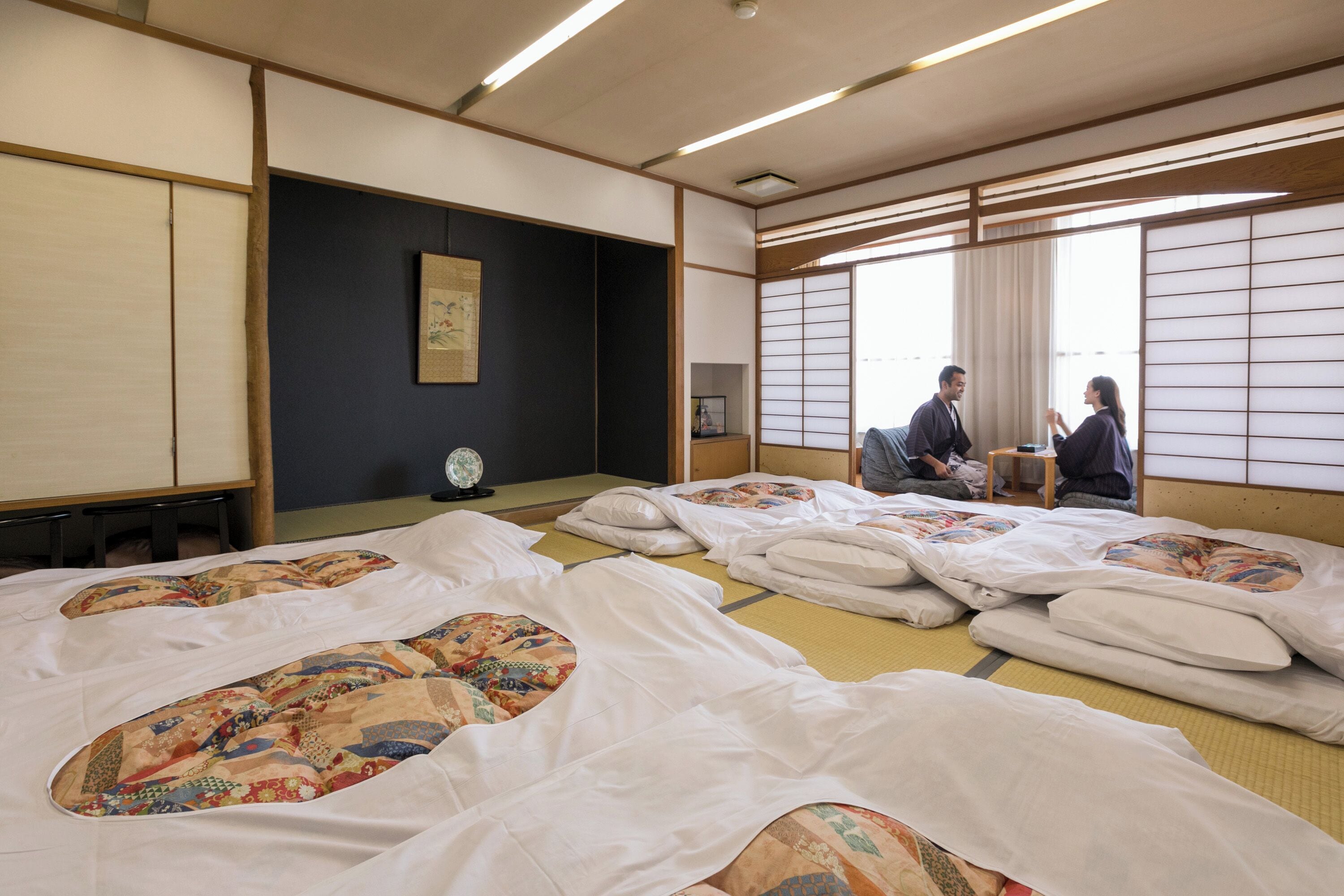 A traditional Japanese room with tatami mats, shoji screens, and a tatami mat bed with a colorful quilt.
